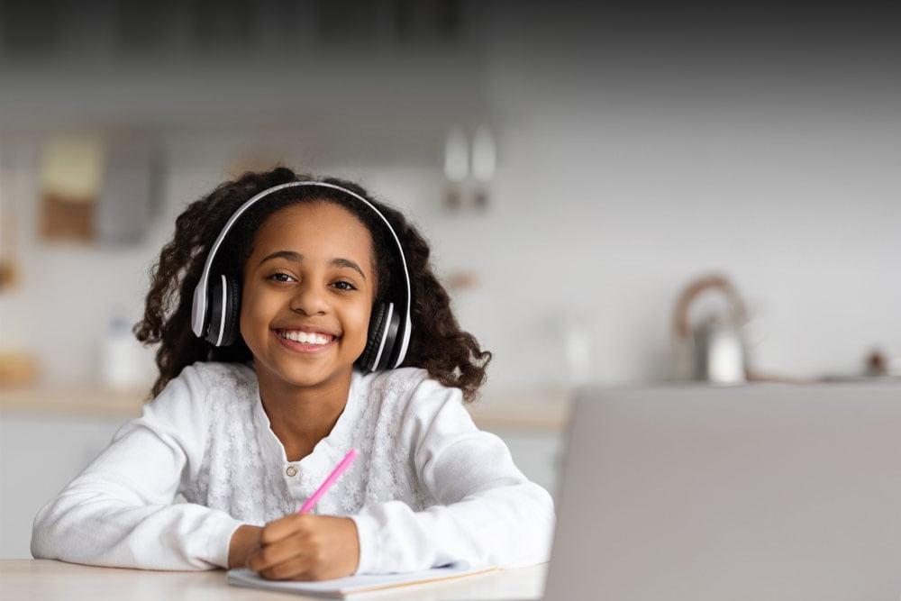 一个穿着白衬衫的女孩微笑着在学校日记上写着，她在激励联系学院上在线课程. 